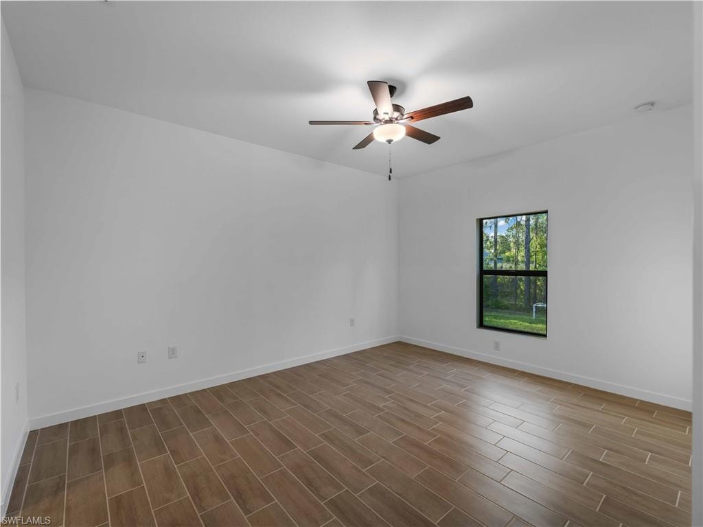 Unfurnished room with a ceiling fan, dark wood-style flooring, baseboards, and a smoke detector