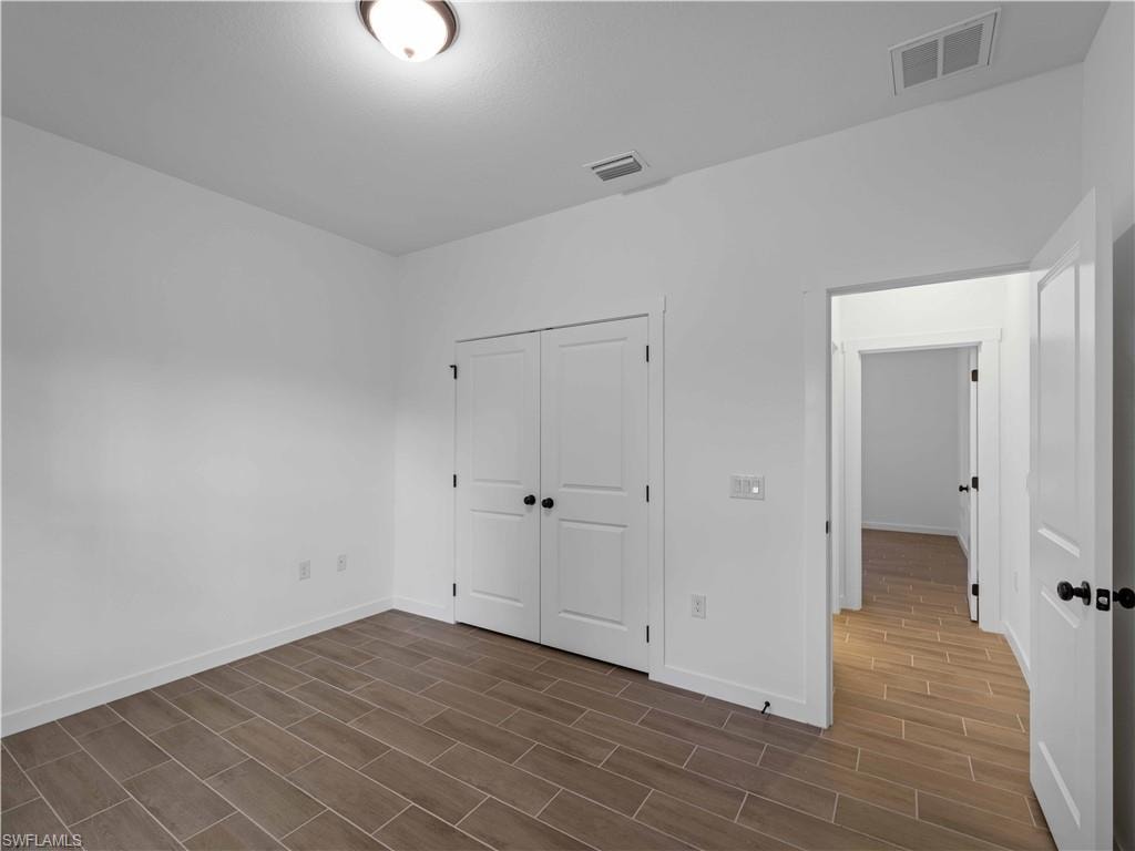 Unfurnished bedroom with dark wood-style flooring, baseboards, and a closet