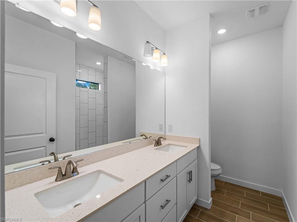 Full bathroom with toilet, wood finish floors, baseboards, double vanity, and recessed lighting