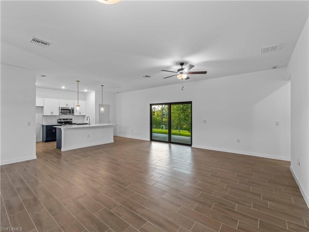 Unfurnished living room featuring ceiling fan, baseboards, wood finished floors, recessed lighting, and a sink