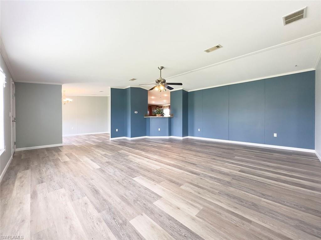 Unfurnished living room with crown molding, light wood-type flooring, and ceiling fan with notable chandelier