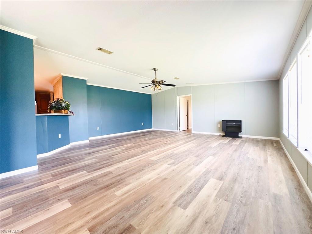 Unfurnished living room with light hardwood / wood-style floors, crown molding, and ceiling fan