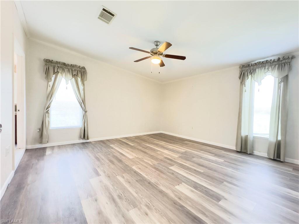 Empty room featuring a healthy amount of sunlight, wood-type flooring, crown molding, and ceiling fan