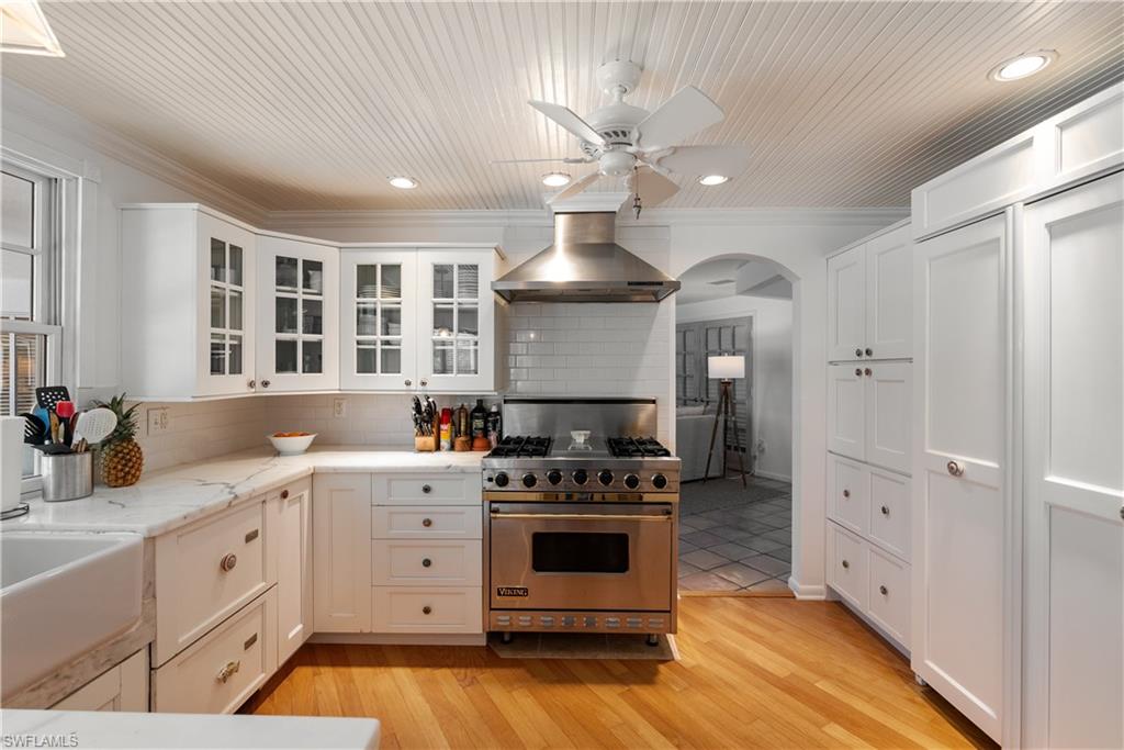 Kitchen with premium range, light hardwood / wood-style floors, ceiling fan, tasteful backsplash, and wall chimney exhaust hood