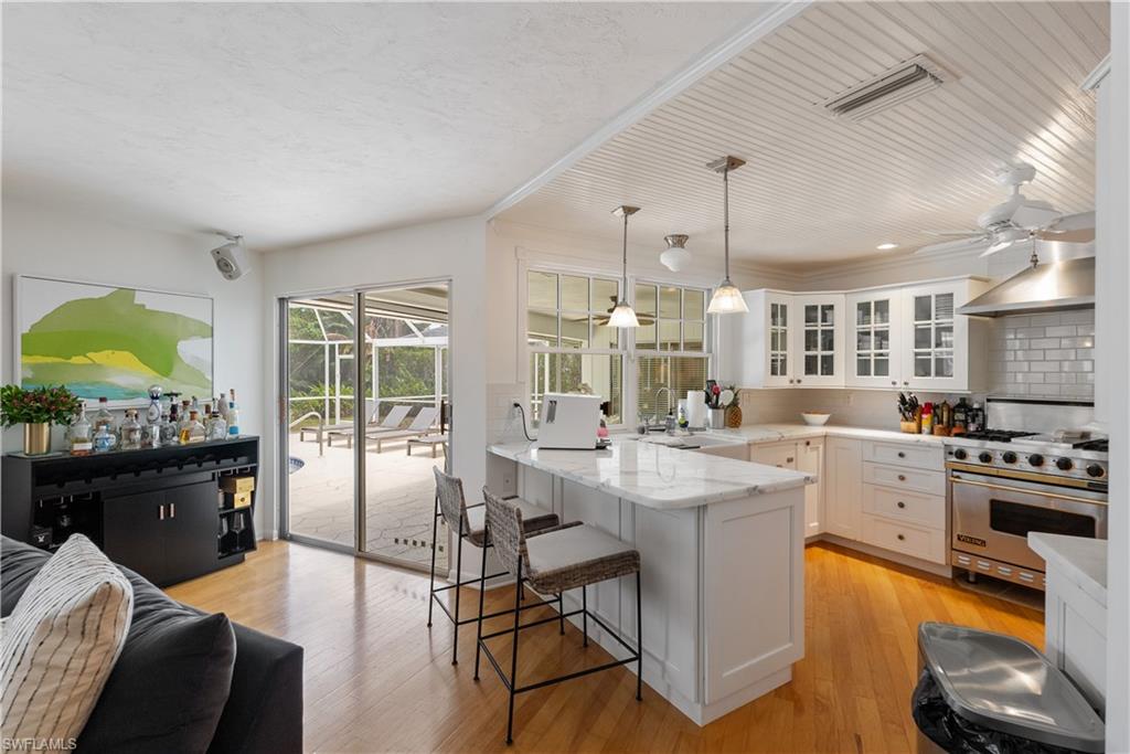 Kitchen featuring designer range, light wood-type flooring, wall chimney exhaust hood, white cabinets, and sink