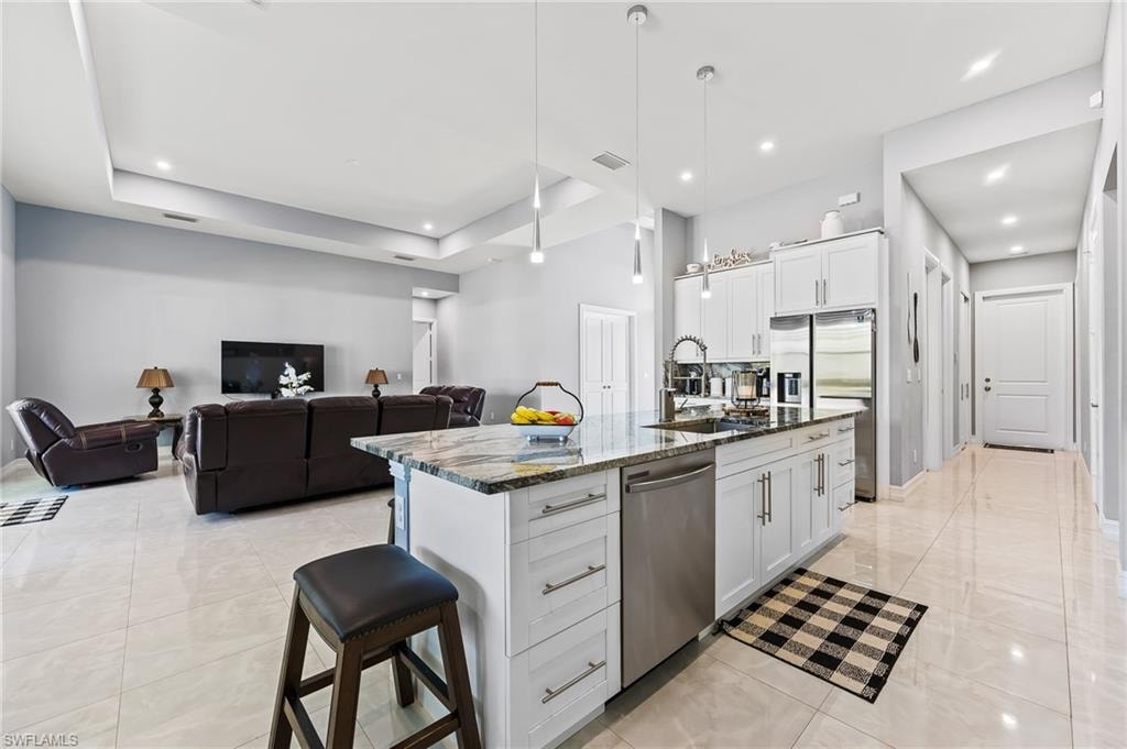 Kitchen with white cabinetry, hanging light fixtures, an island with sink, appliances with stainless steel finishes, and a raised ceiling