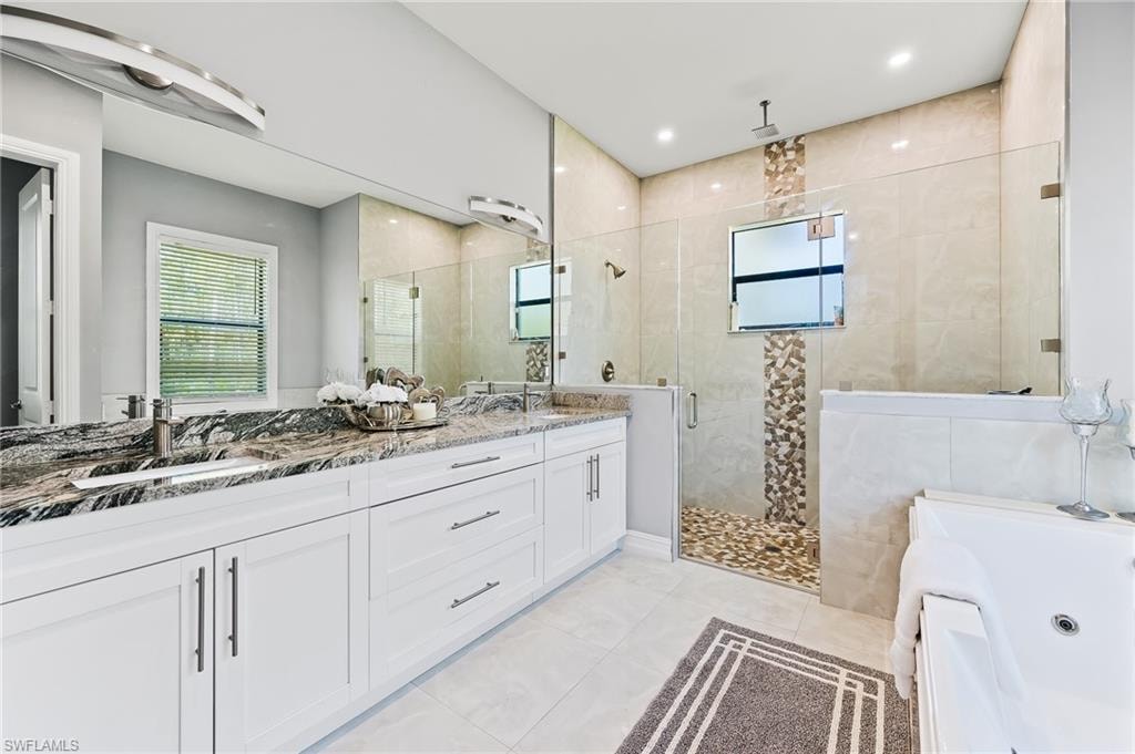 Bathroom featuring oversized vanity, double sink, tile walls, plus walk in shower, and tile floors