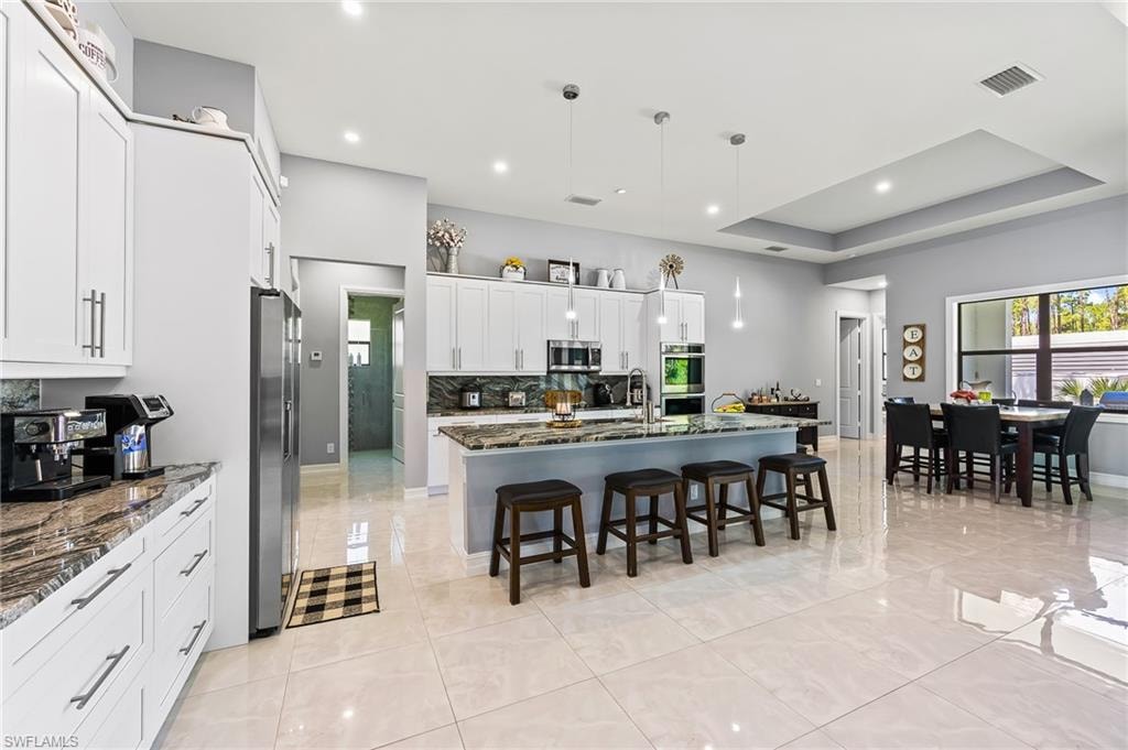 Kitchen featuring stainless steel appliances, hanging light fixtures, a center island with sink, and dark stone counters