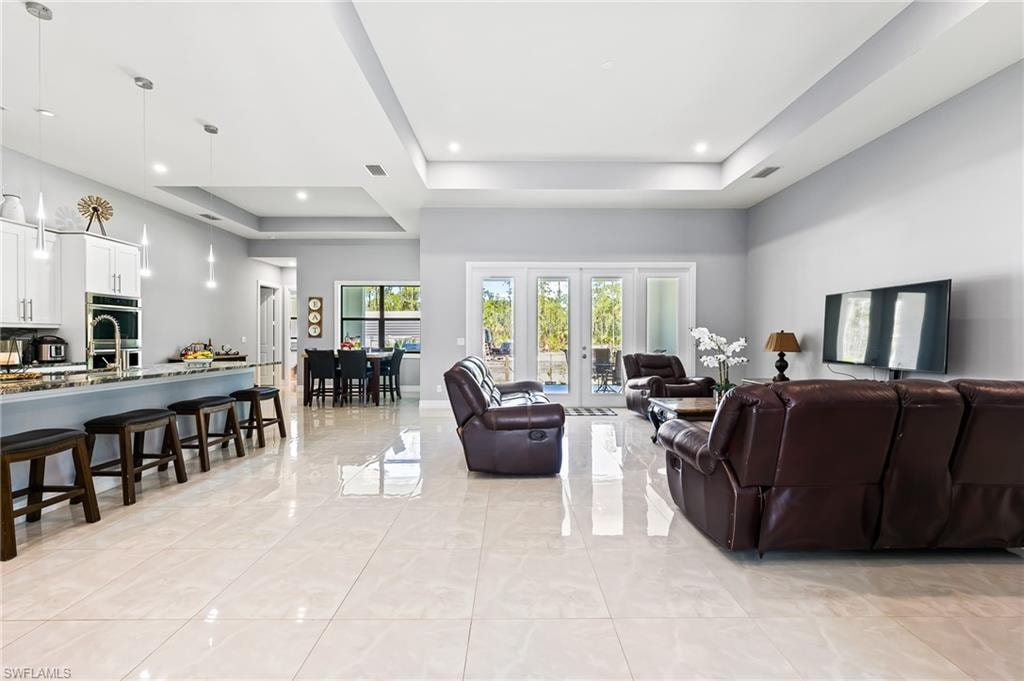 Living room with a tray ceiling, french doors, and light tile floors