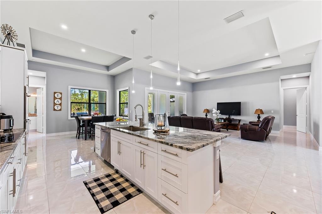 Kitchen featuring a raised ceiling, light tile flooring, a kitchen island with sink, and sink