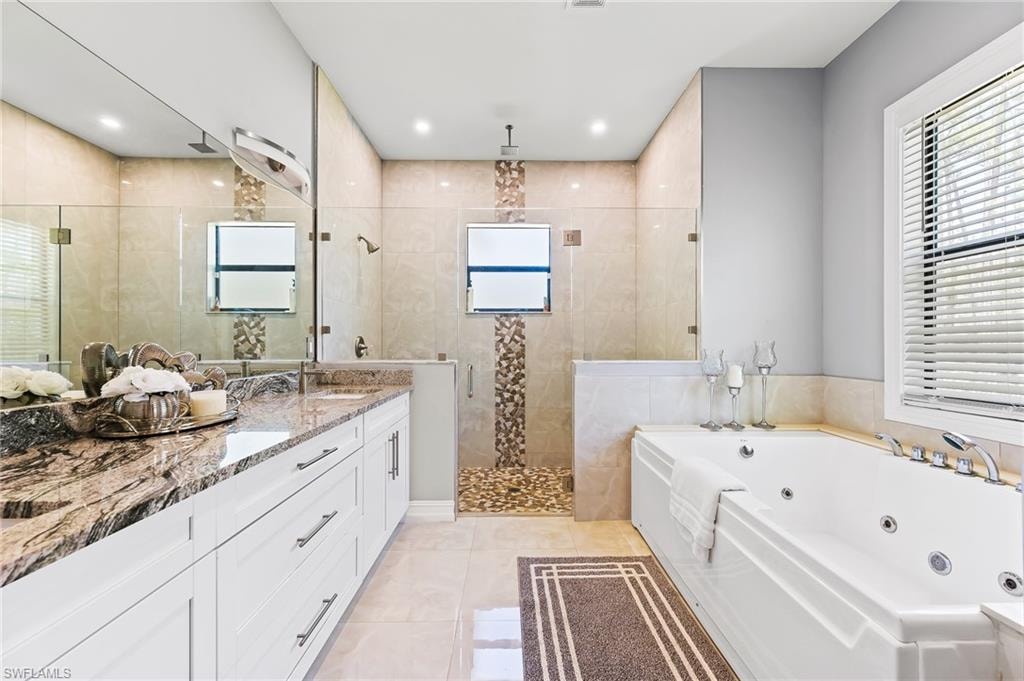 Bathroom featuring tile walls, tile flooring, dual vanity, and separate shower and tub
