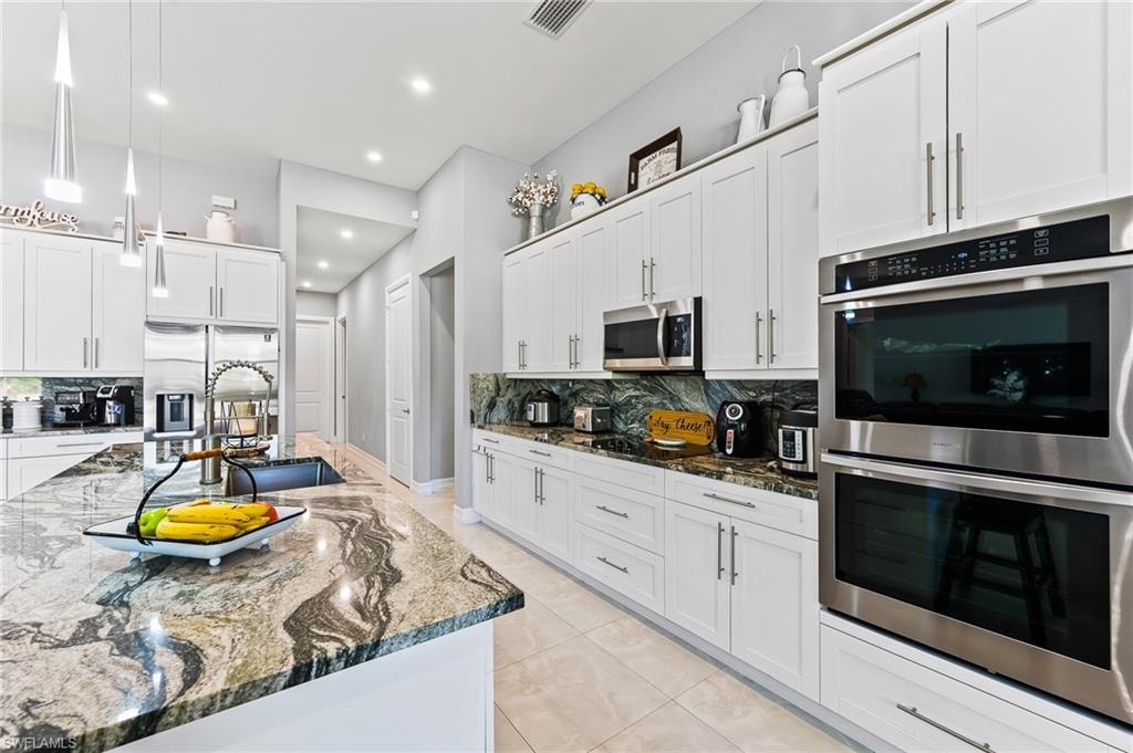 Kitchen featuring stainless steel appliances, hanging light fixtures, tasteful backsplash, and white cabinets