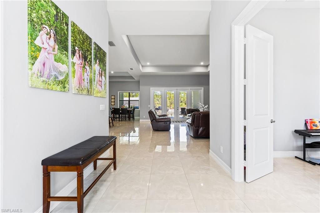 Corridor featuring a tray ceiling, light tile flooring, and french doors