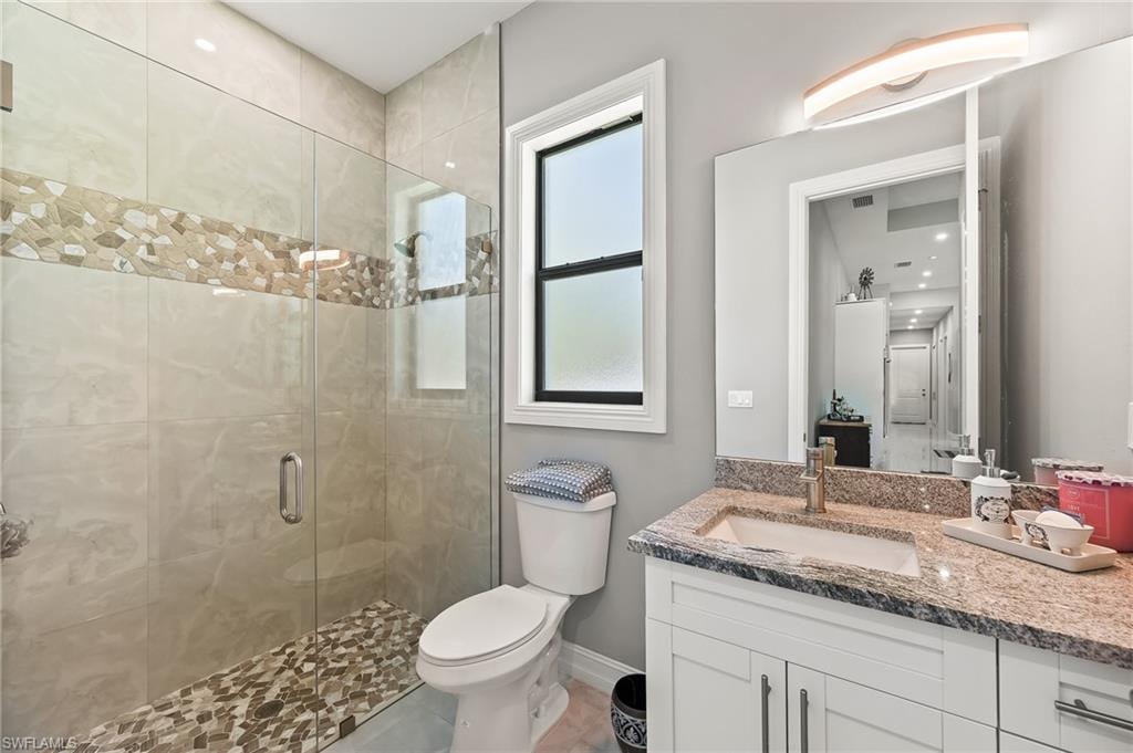 Bathroom with an enclosed shower, oversized vanity, tile flooring, and toilet