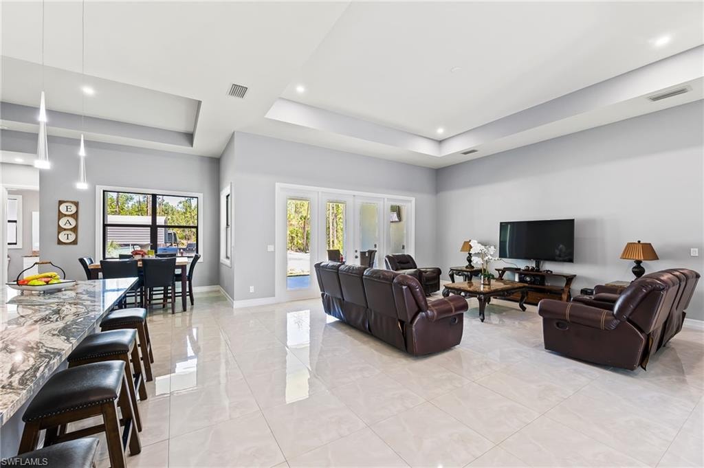 Living room featuring a raised ceiling, french doors, and light tile floors