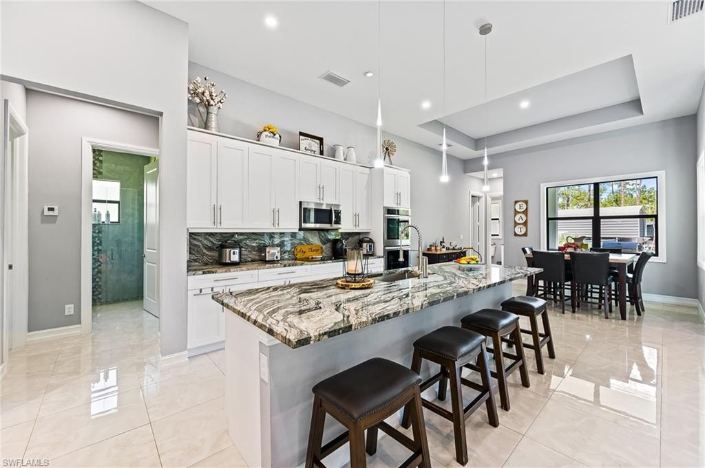 Kitchen featuring appliances with stainless steel finishes, white cabinetry, an island with sink, and pendant lighting