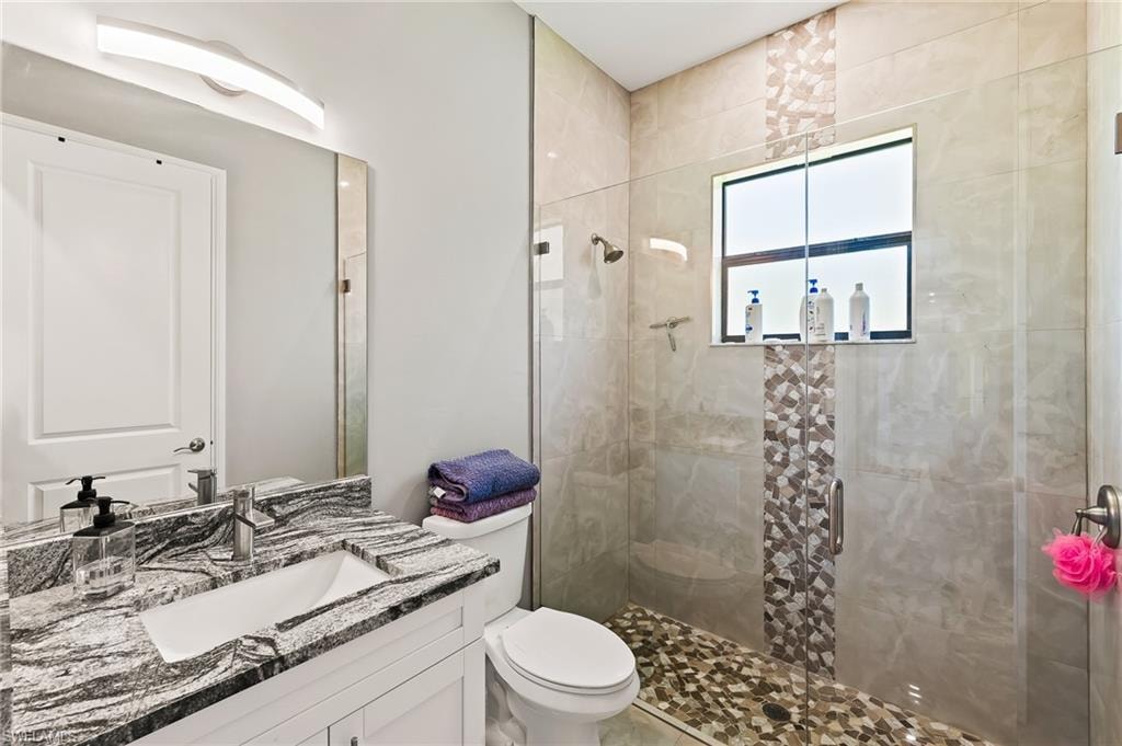 Bathroom featuring a shower with door, toilet, and large vanity