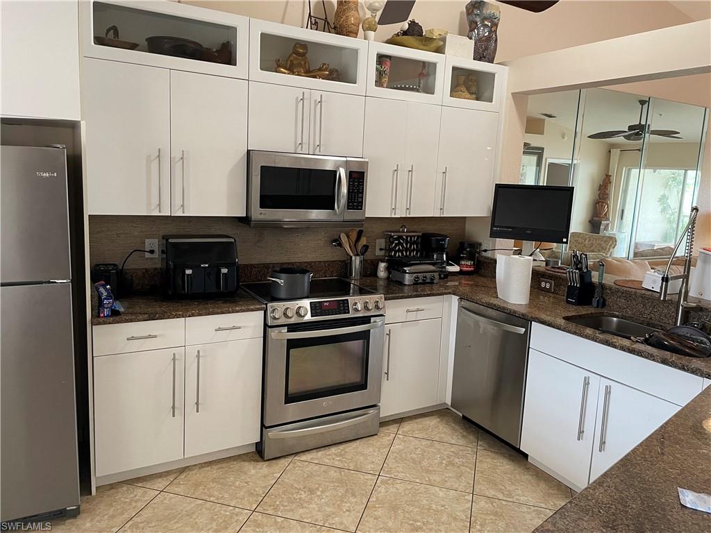 Kitchen featuring ceiling fan, stainless steel appliances, light tile flooring, backsplash, and white cabinets