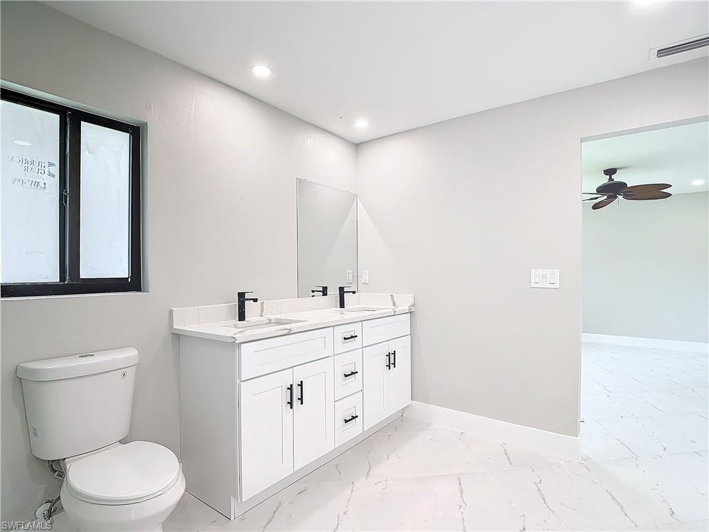 Bathroom with tile flooring, double sink, vanity with extensive cabinet space, ceiling fan, and toilet