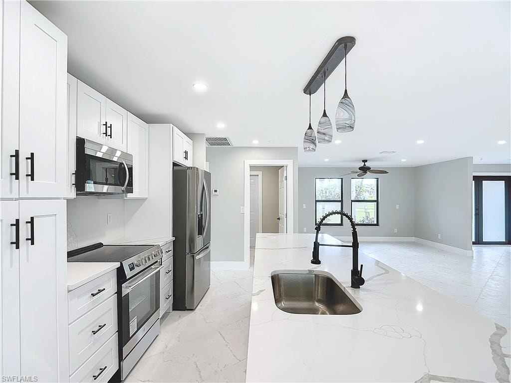 Kitchen with appliances with stainless steel finishes, white cabinetry, sink, and pendant lighting