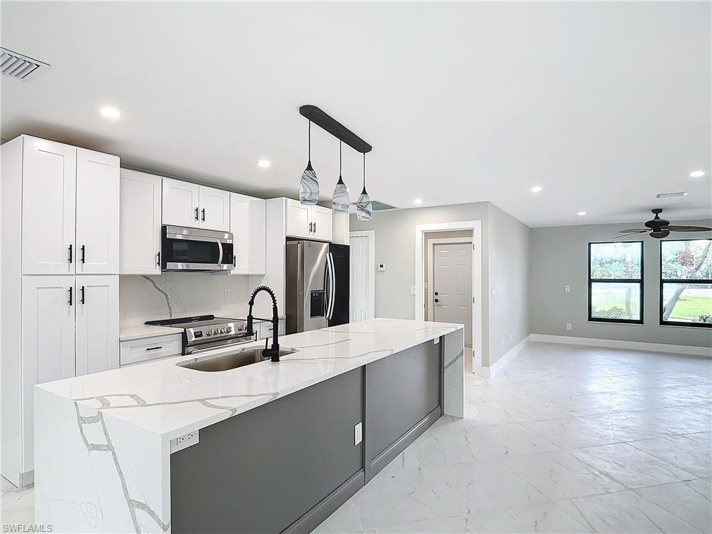 Kitchen featuring decorative light fixtures, appliances with stainless steel finishes, ceiling fan, and white cabinets