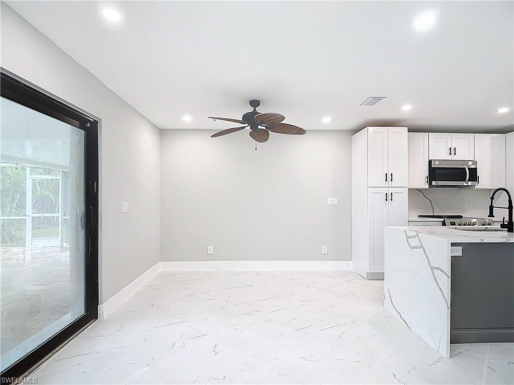 Kitchen with white cabinets, light tile flooring, ceiling fan, and light stone countertops