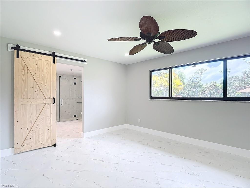 Empty room featuring a barn door, ceiling fan, and light tile flooring
