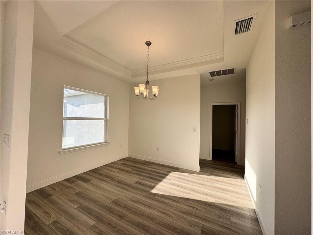 Empty room featuring a raised ceiling, dark wood finished floors, a chandelier, and baseboards