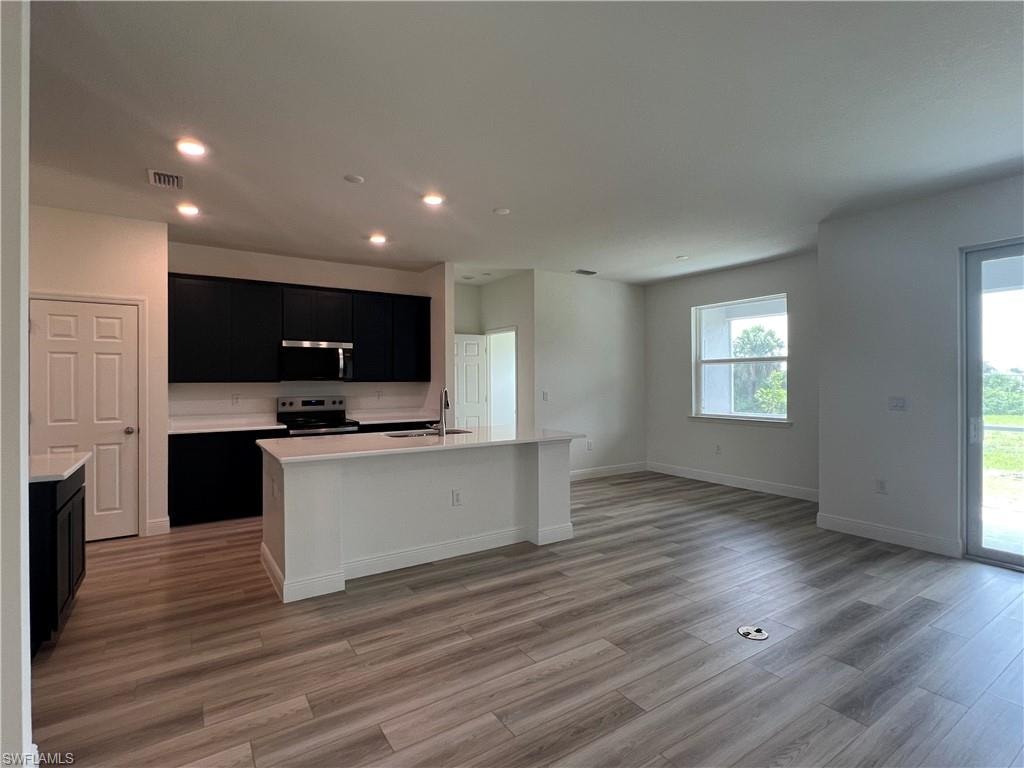 Kitchen featuring dark cabinetry, open floor plan, light countertops, appliances with stainless steel finishes, and recessed lighting
