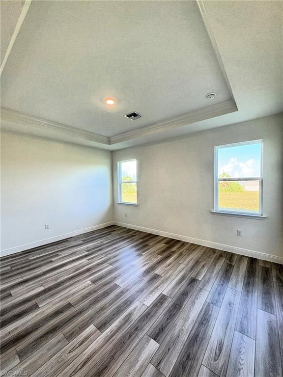 Empty room with ornamental molding, a tray ceiling, dark wood-style floors, baseboards, and a textured ceiling