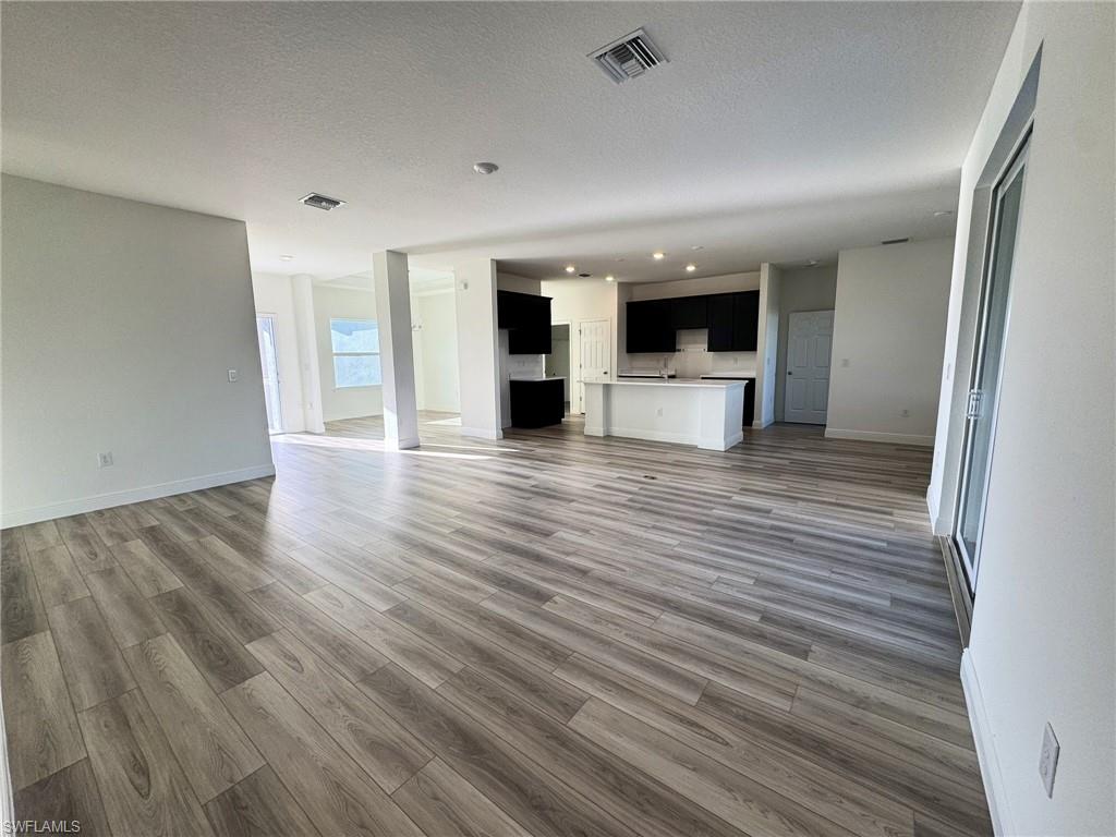 Unfurnished living room featuring wood finished floors, recessed lighting, baseboards, and a textured ceiling