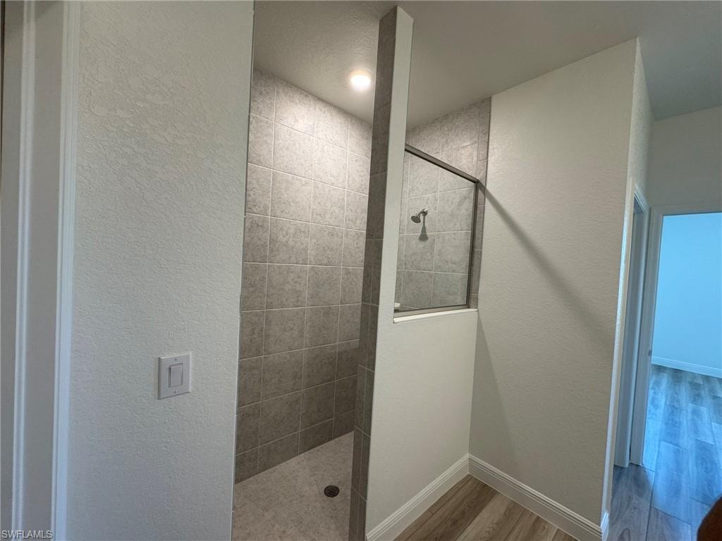 Bathroom featuring wood finished floors, walk in shower, and baseboards