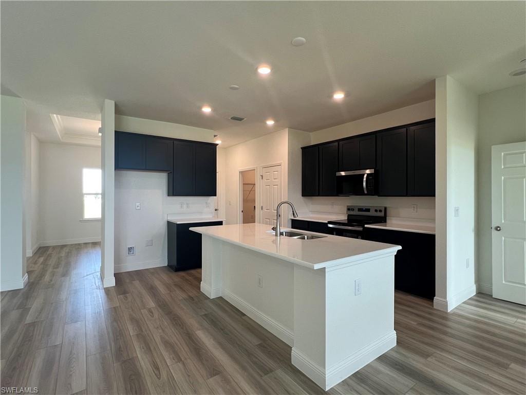 Kitchen featuring dark cabinets, an island with sink, stainless steel appliances, light wood-type flooring, and recessed lighting