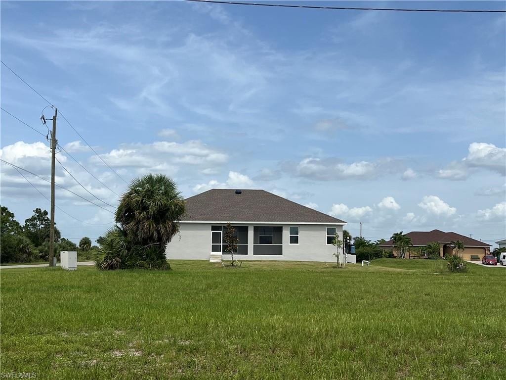 Rear view of property with a lawn, stucco siding, and roof with shingles