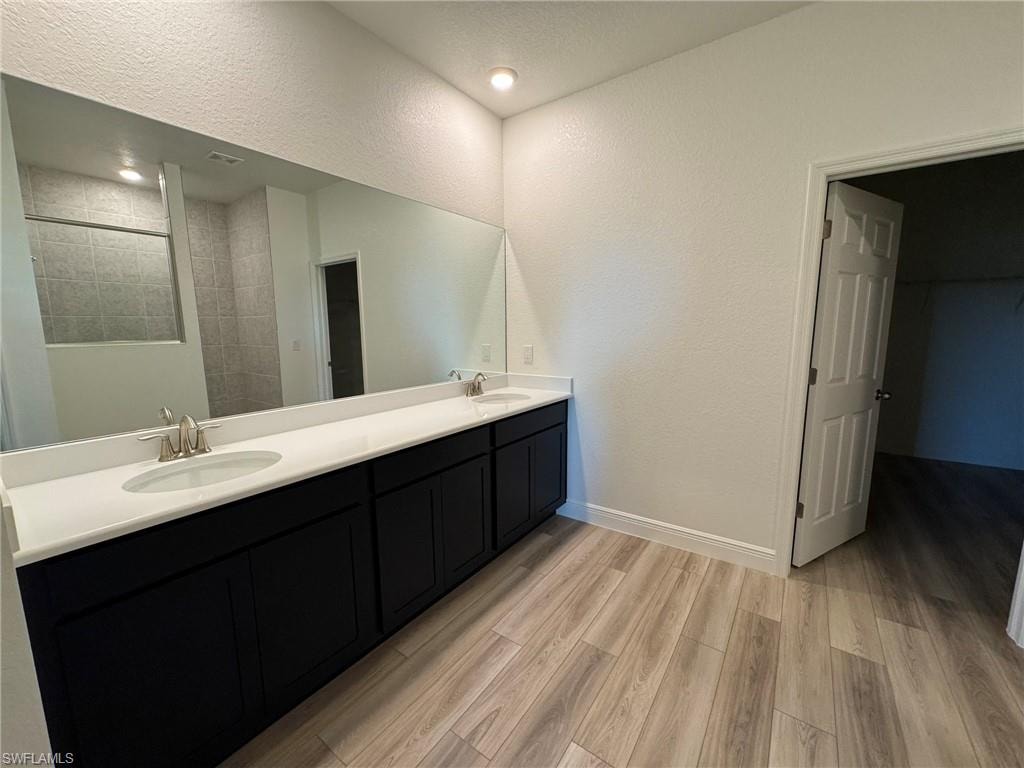 Full bathroom with double vanity, wood finished floors, baseboards, and a tile shower