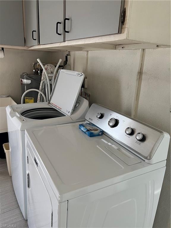 Laundry room featuring washer and clothes dryer, light tile patterned floors, and cabinets