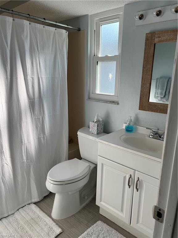Full bathroom with a textured ceiling, toilet, vanity, and shower / bathtub combination with curtain