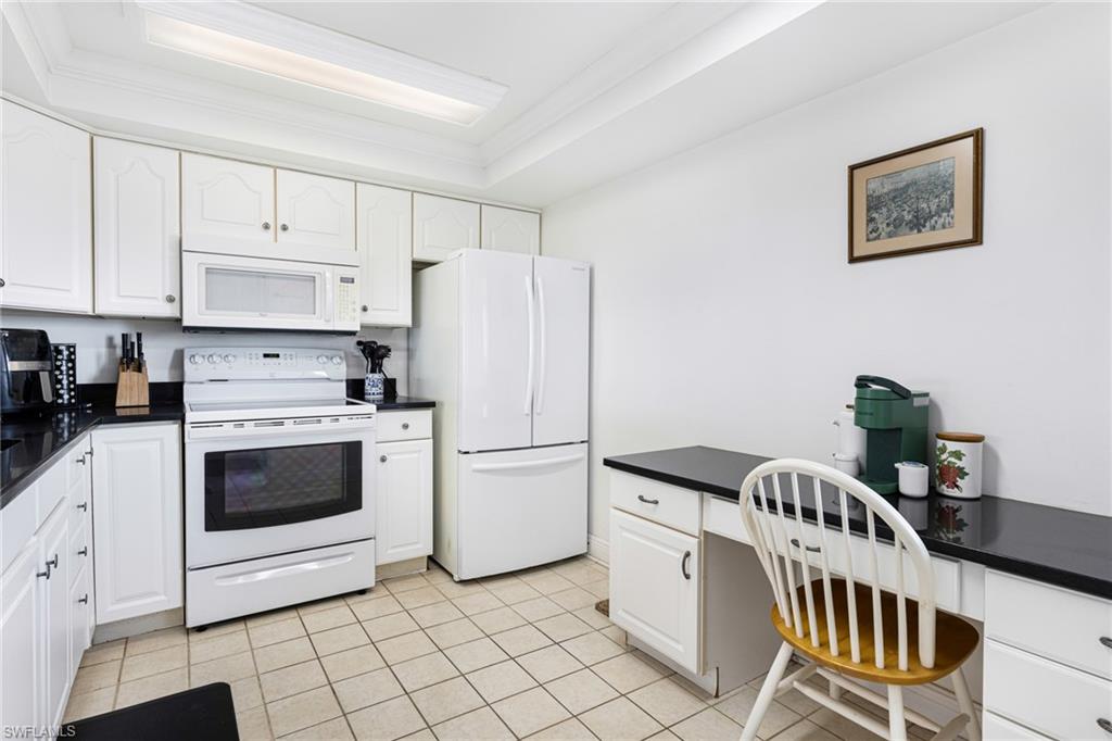 Kitchen featuring light tile patterned floors, white cabinetry, white appliances, and a raised ceiling