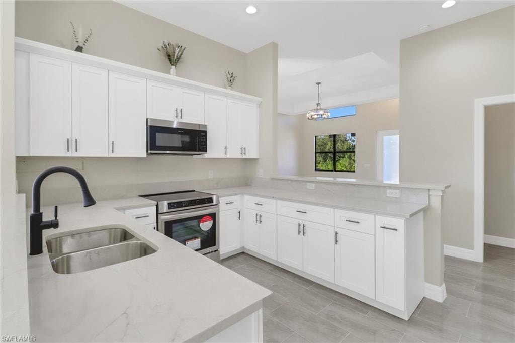 Kitchen with pendant lighting, white cabinets, sink, kitchen peninsula, and stainless steel appliances