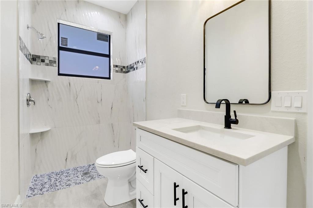 Bathroom with a tile shower, vanity, and toilet