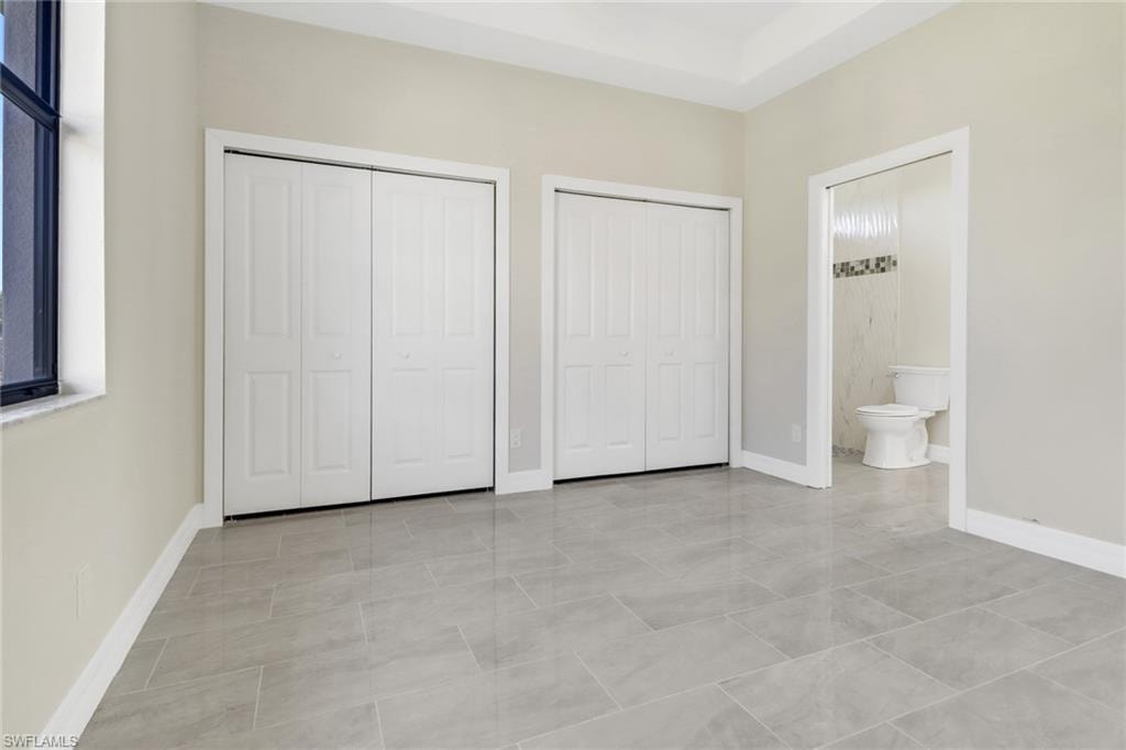 Unfurnished bedroom featuring light tile patterned floors, connected bathroom, and two closets