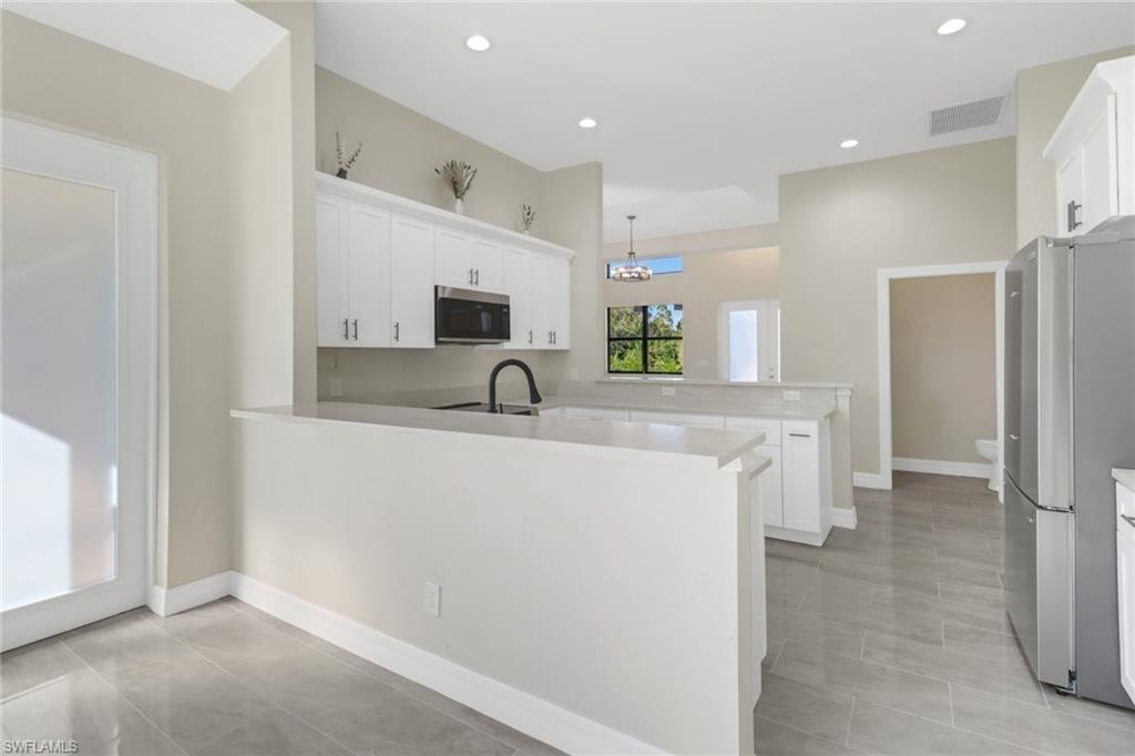 Kitchen featuring pendant lighting, an inviting chandelier, white cabinets, appliances with stainless steel finishes, and kitchen peninsula