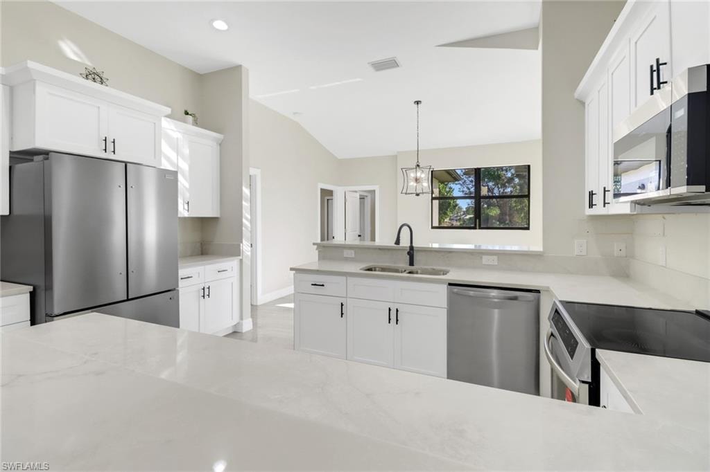 Kitchen featuring sink, white cabinets, stainless steel appliances, and decorative light fixtures