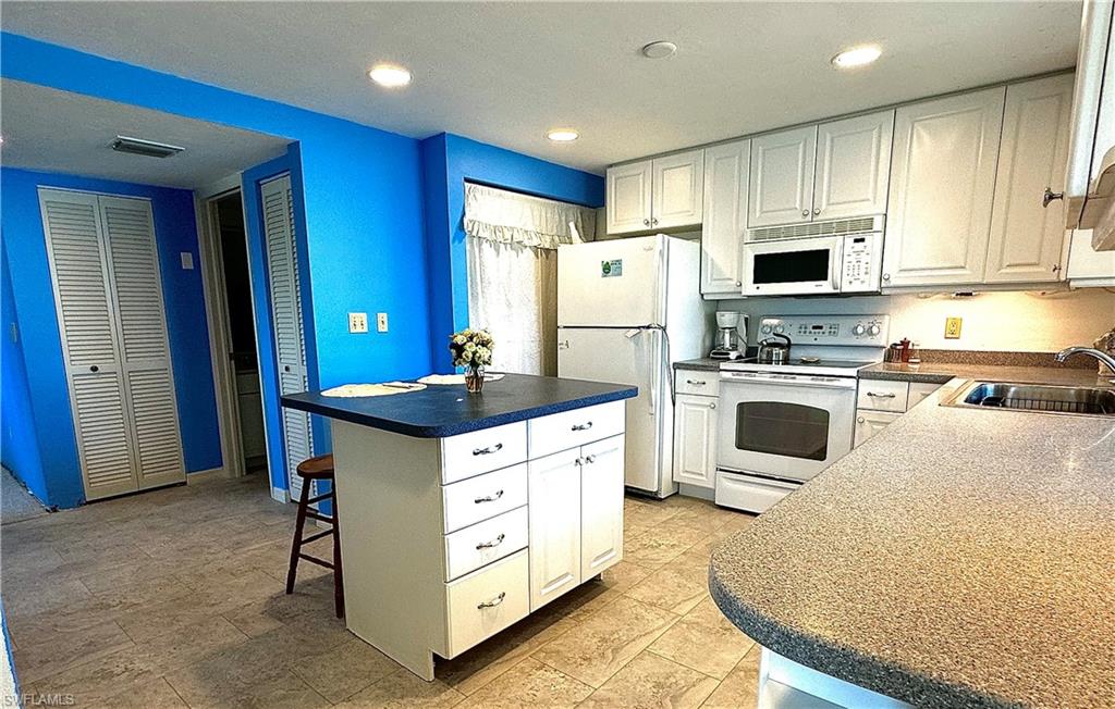 Kitchen with sink, light tile patterned flooring, white cabinets, and white appliances