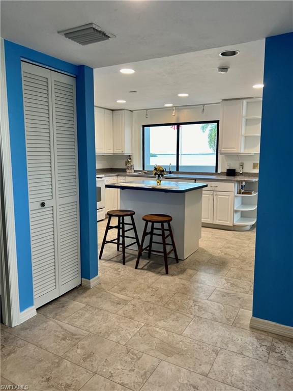 Kitchen with a kitchen bar, stove, a kitchen island, light tile patterned flooring, and white cabinetry