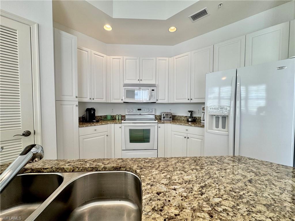 Kitchen with white cabinets, granite countertops, white appliances, and sink