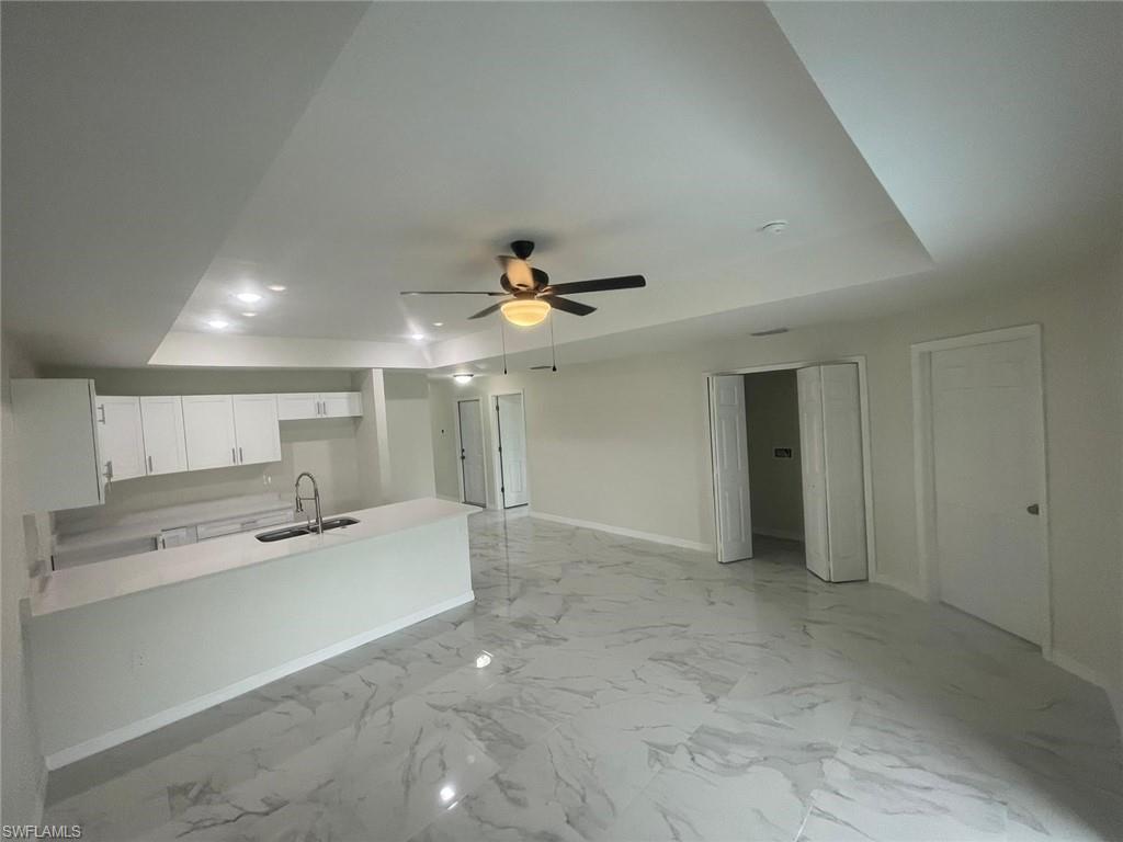 Kitchen with white cabinets, kitchen peninsula, sink, ceiling fan, and a tray ceiling