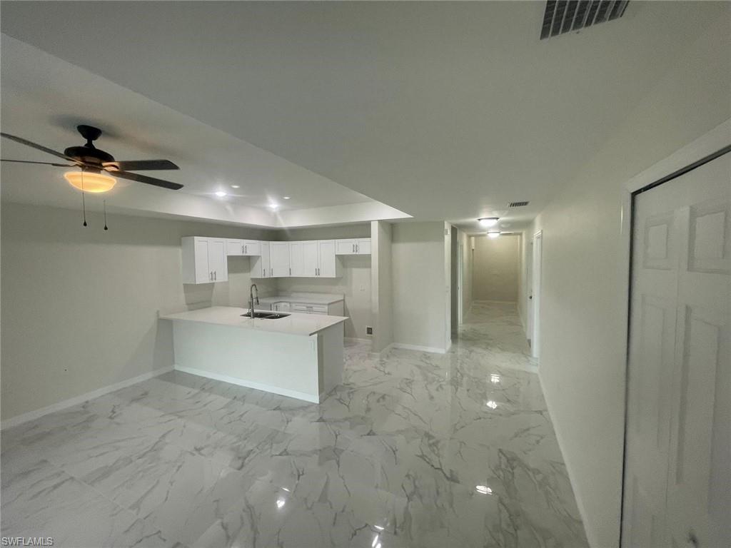 Kitchen with white cabinets, ceiling fan, sink, and kitchen peninsula