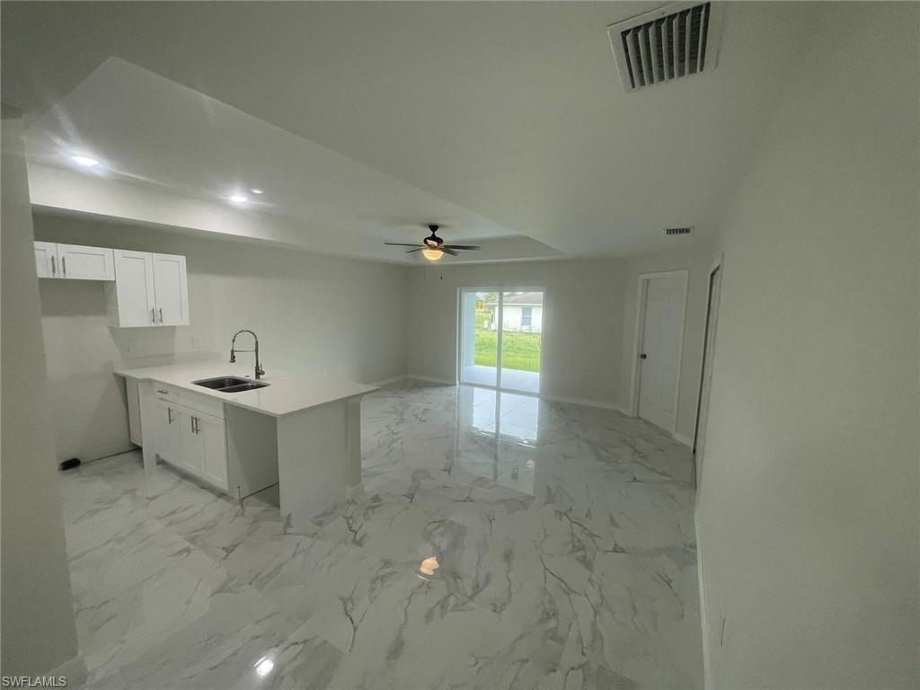 Kitchen featuring kitchen peninsula, sink, ceiling fan, and white cabinets
