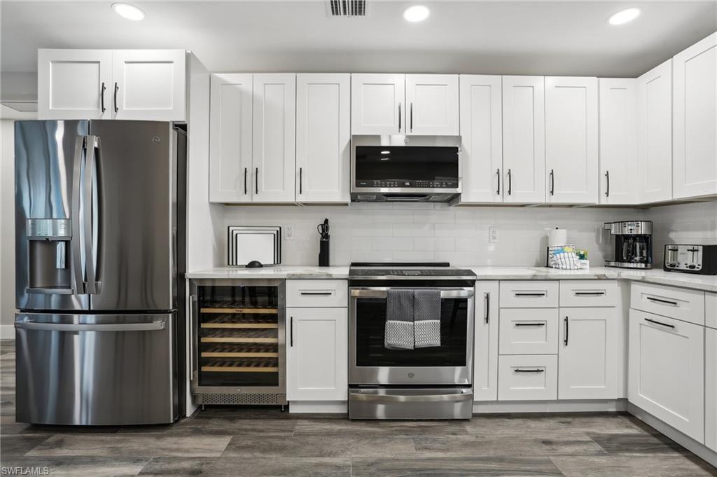 Kitchen featuring white cabinets, wine cooler, appliances with stainless steel finishes, backsplash, and dark wood-type flooring